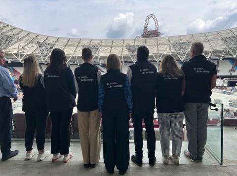 Seven of the Mates in Mind team looking at the pitch in the London Stadium, with ‘be a mate, be the change’ on their backs