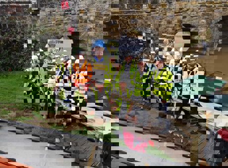 Eleven construction workers wearing hard hats and high vis jackets, standing on a riverbank with a Mates in Mind banner behind them