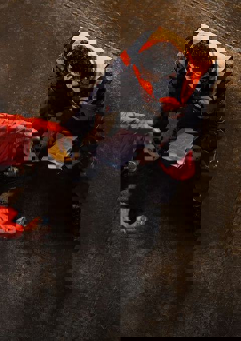 Looking down on two men wearing high vis clothing, sitting on boxes in a warehouse, talking about their mental health